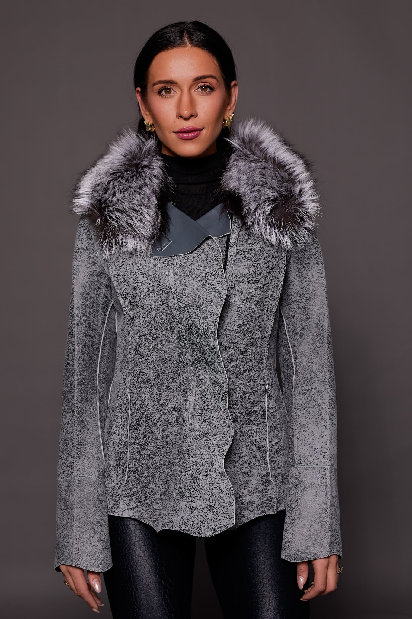 Frontal view of a woman in a grey leather jacket standing in front of a dark grey background.