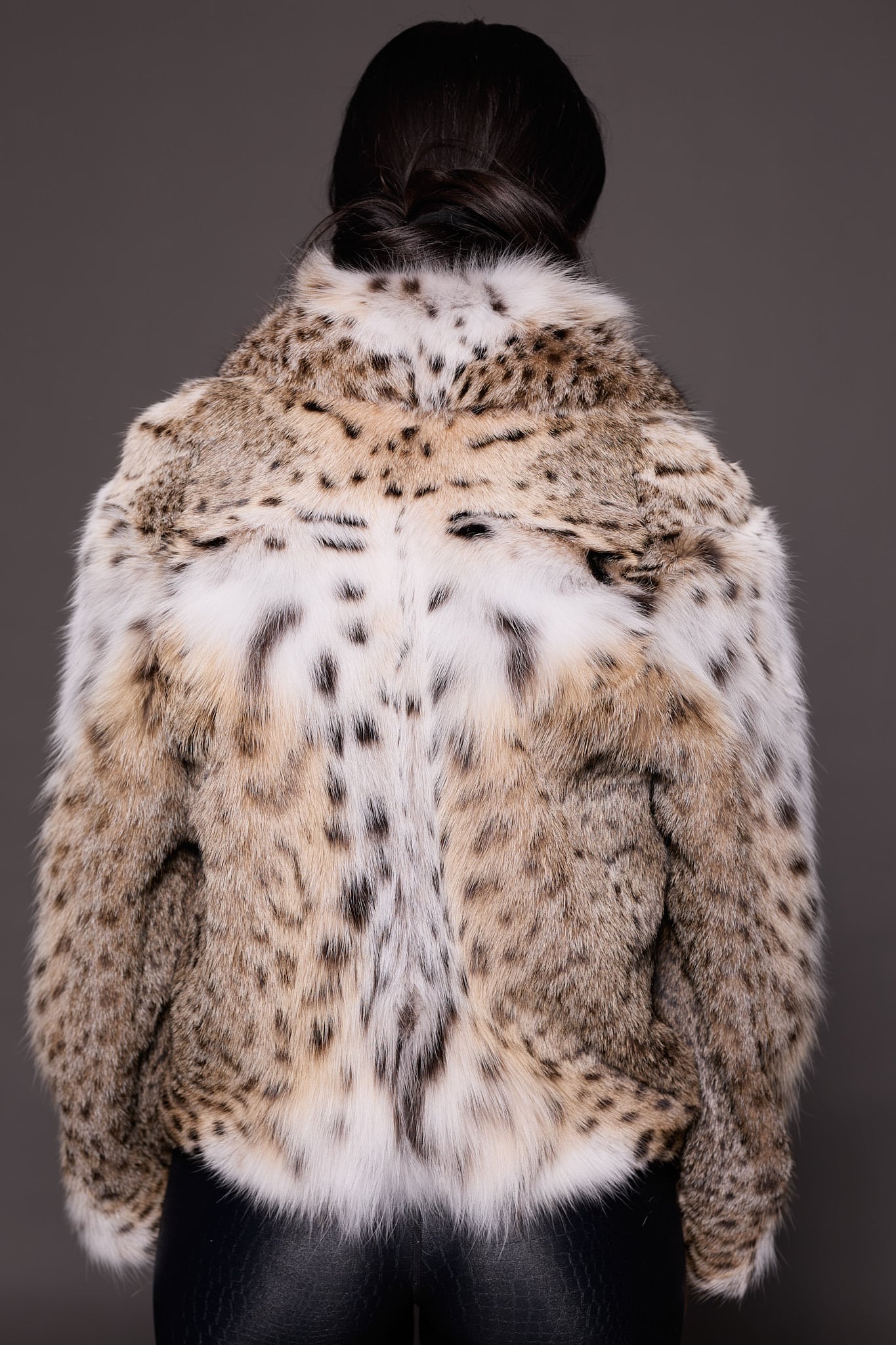 the back of a woman in a lynx fur coat against a grey background