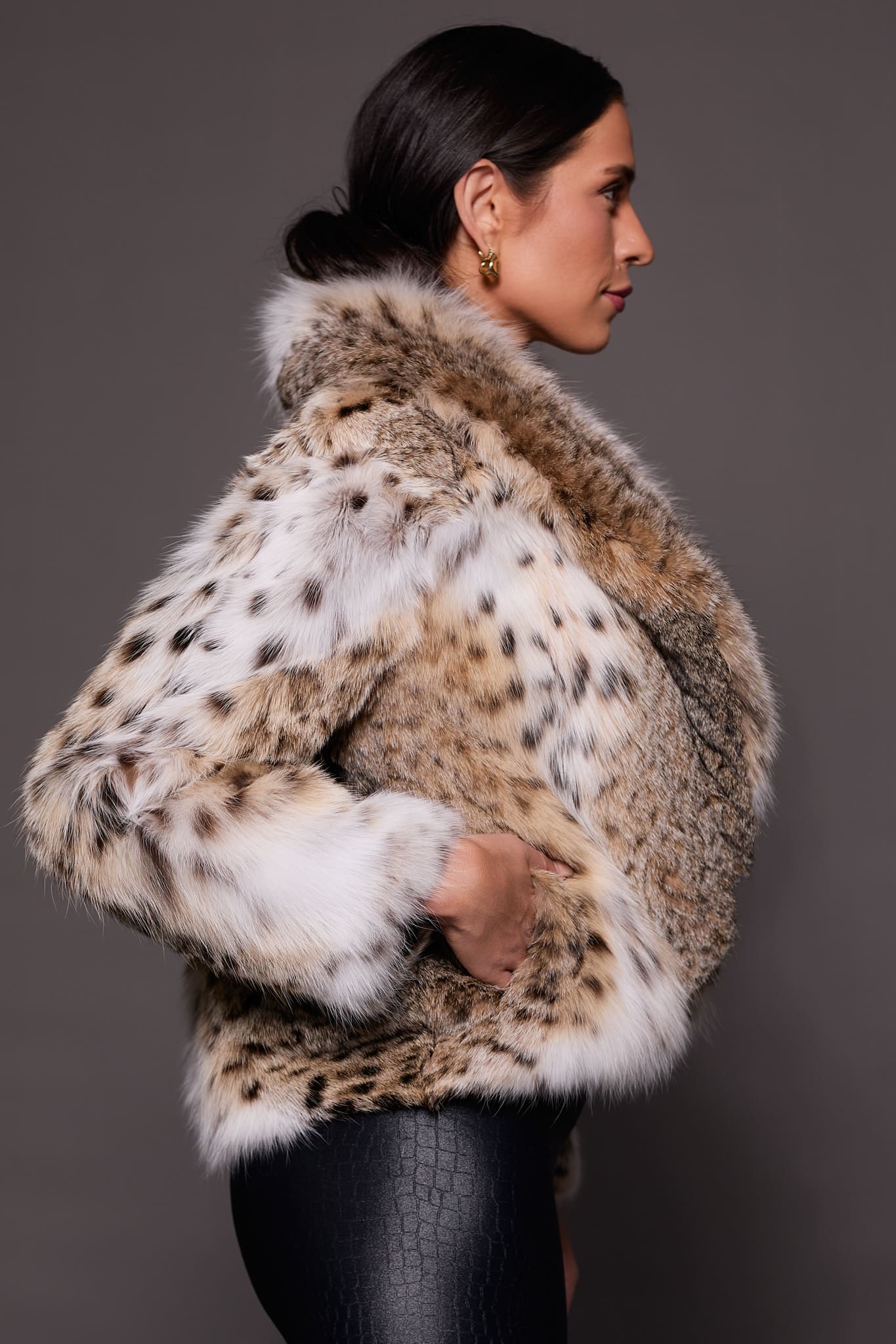 the side of a woman in a lynx fur coat against a grey background