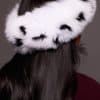 Rear view close up of the back of a woman's head. The woman is wearing a spotted fox fur headband and facing a grey background.