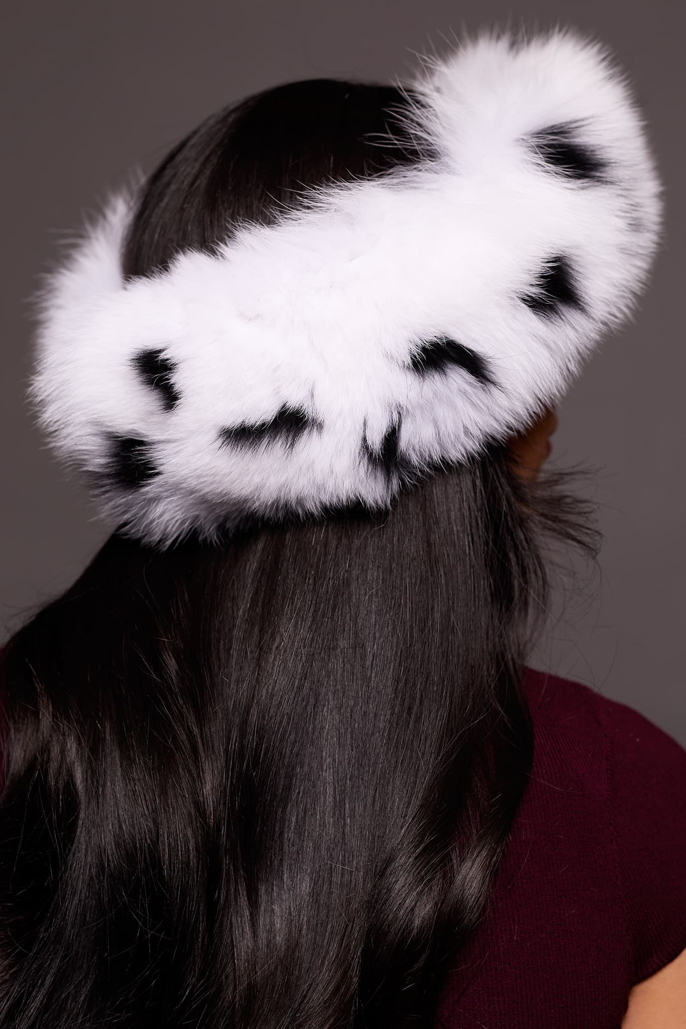 Rear view close up of the back of a woman's head. The woman is wearing a spotted fox fur headband and facing a grey background.