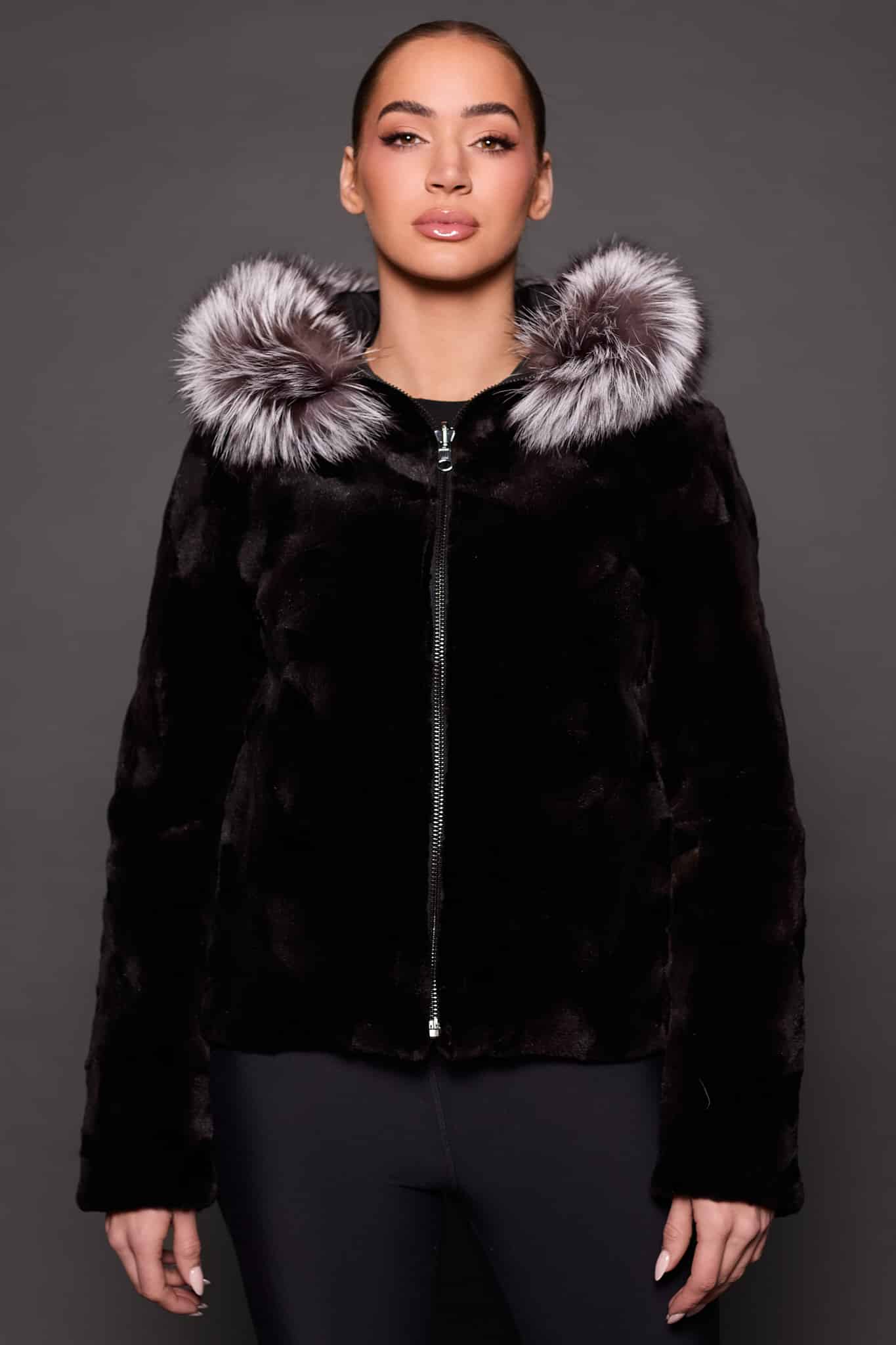 GIA MINK BLACK SILVER FOX FRONT the front of a woman in a black and grey fur jacket against a grey background