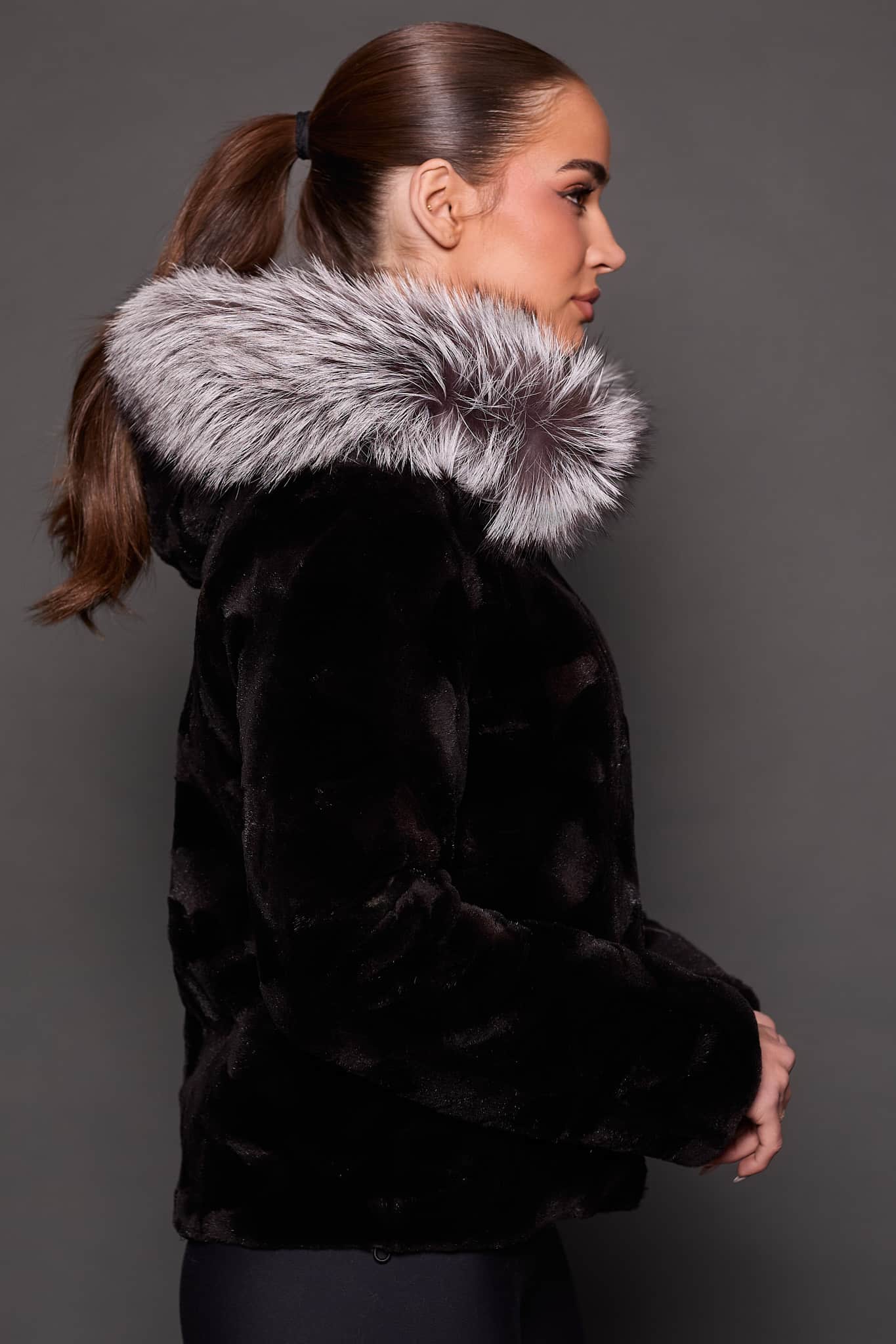 GIA MINK BLACK SILVER FOX SIDE the side of a woman in a black and grey fur jacket against a grey background