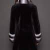 Rear view of a woman wearing a sheared mink fur coat facing a grey background. The woman's head is turned slightly to the right of frame.