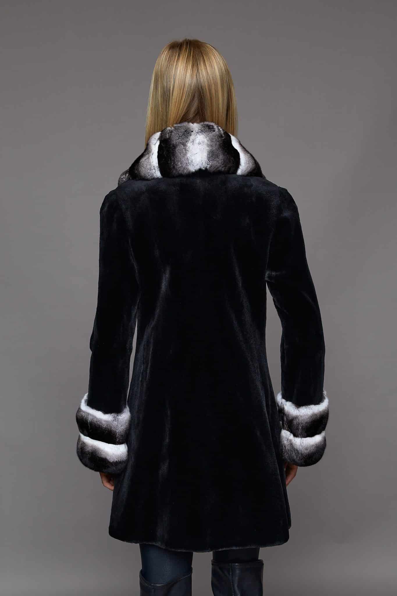 The back of a woman in a black coat with white cuffs in front of a grey background