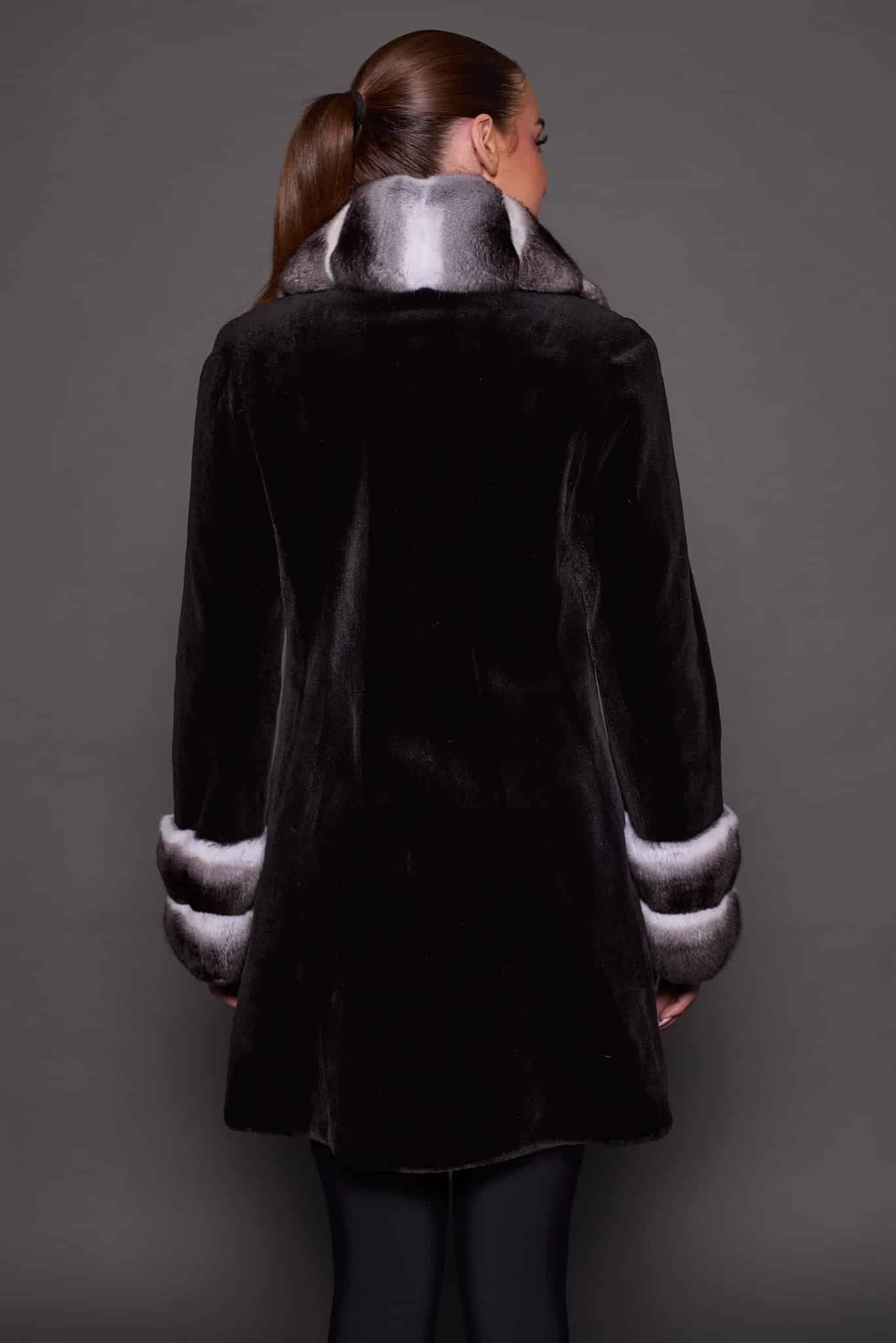 Rear view of a woman wearing a sheared mink fur coat facing a grey background. The woman's head is turned slightly to the right of frame.