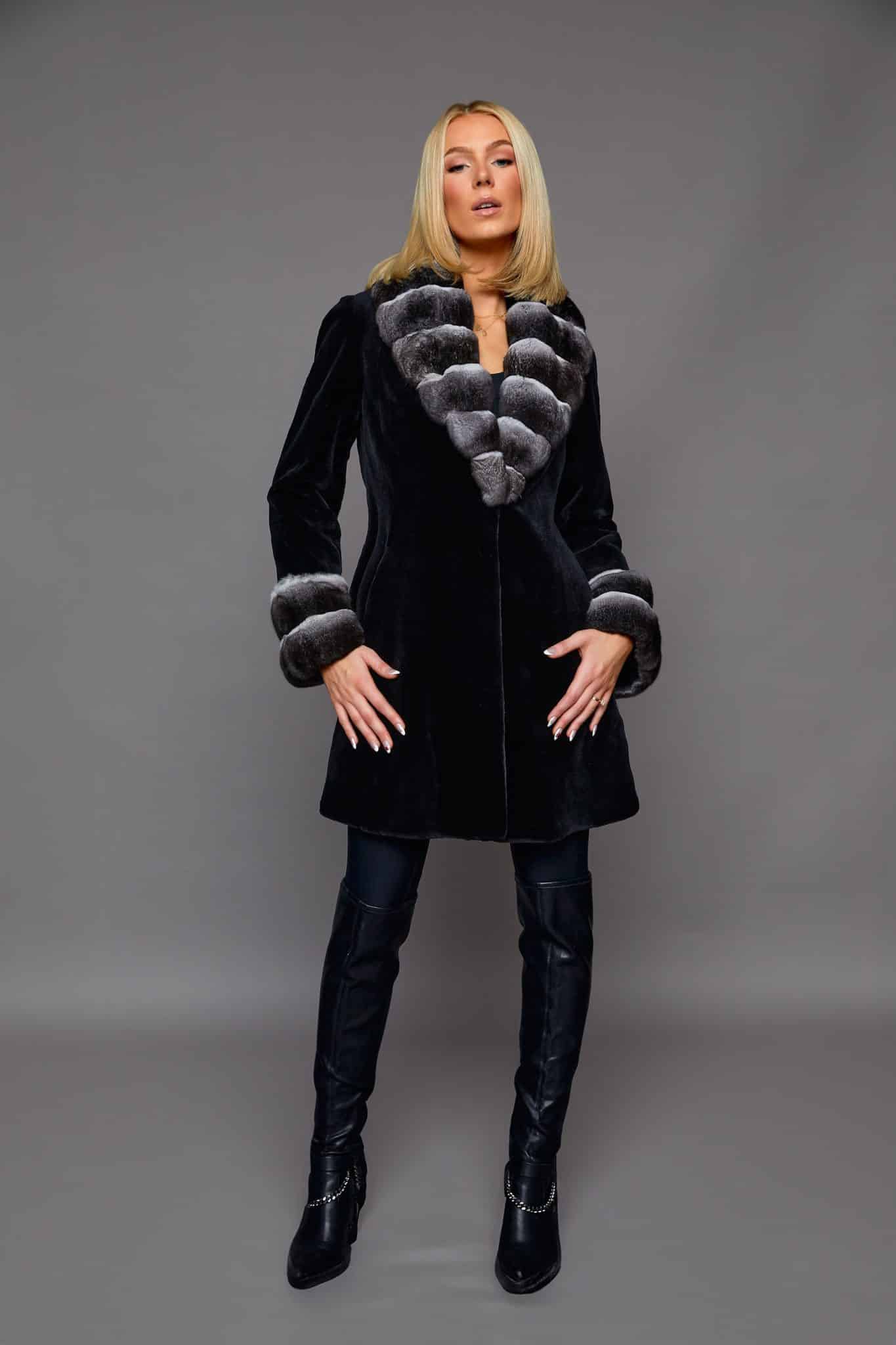 the front of a woman in a black coat with white cuffs in front of a grey background