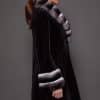 Profile view of a woman wearing a sheared mink fur coat standing in front of a grey background facing the right of frame.