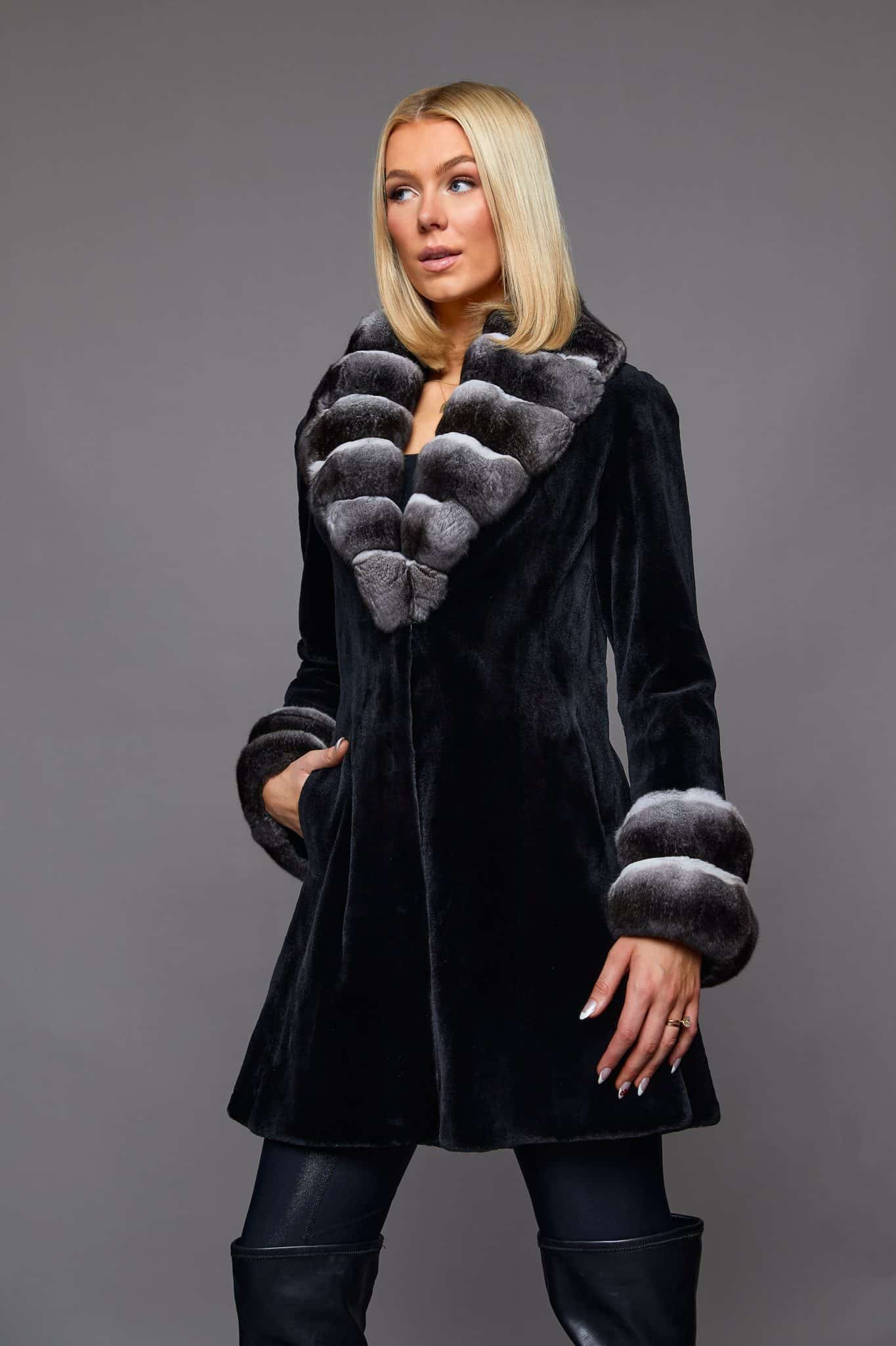 the front of a woman in a black coat with white cuffs in front of a grey background