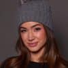 woman wearing a grey knit beanie with a fox puff on the top against a grey background