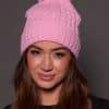 woman wearing a pink knit beanie with a fox puff on the top against a grey background