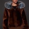 the front image of a woman in a brown jacket with a silver fur trim on the hood against a grey background
