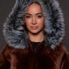up close image of a woman in a brown jacket with a silver fur trim on the hood against a grey background