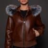 the front image of a woman in a brown jacket with a silver fur trim on the hood against a grey background