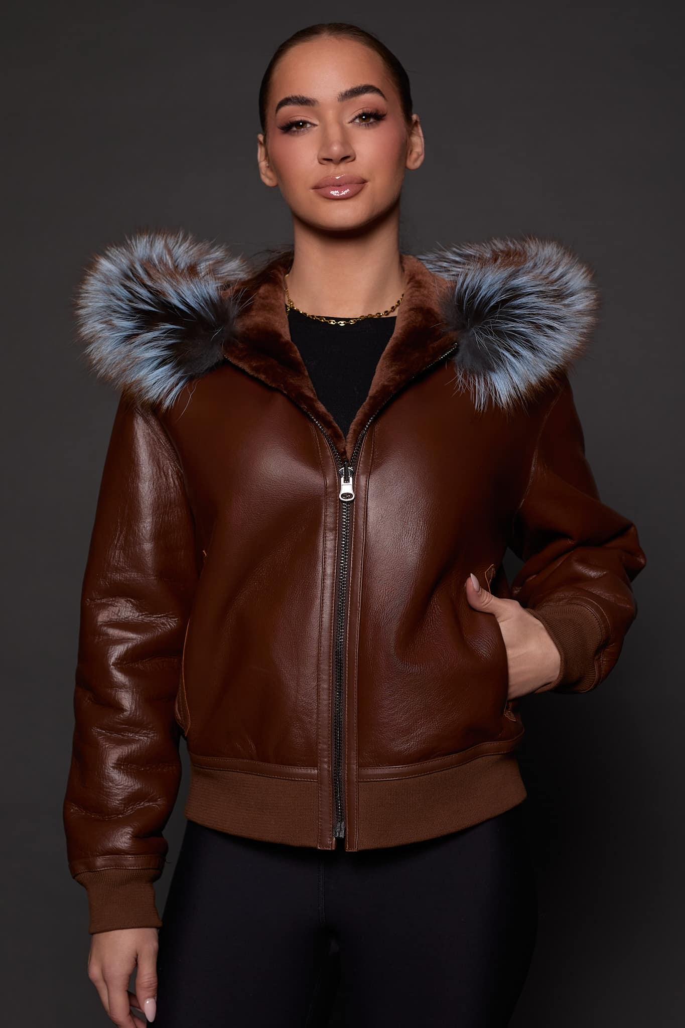 the front image of a woman in a brown jacket with a silver fur trim on the hood against a grey background