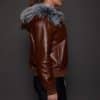 the side profile of a woman in a brown jacket with a silver fur trim on the hood against a grey background