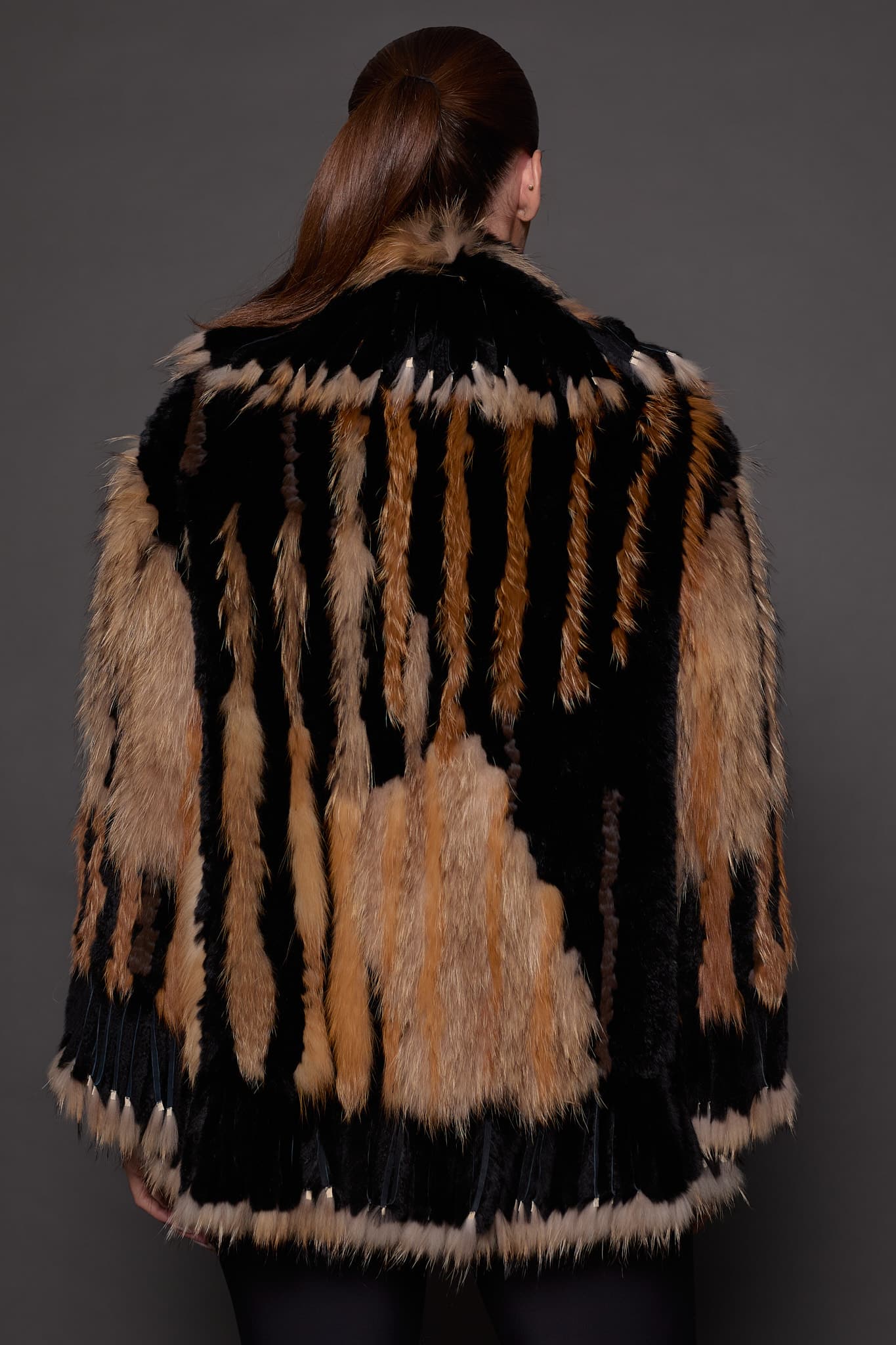 SASCHA REX KNIT BLACK BACK the back of a woman in a black and brown fur knitted jacket against a grey background