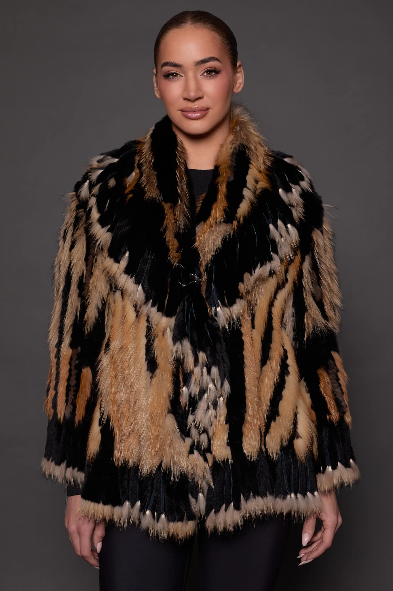 SASCHA REX KNIT BLACK FRONT the front of a woman in a black and brown fur knitted jacket against a grey background