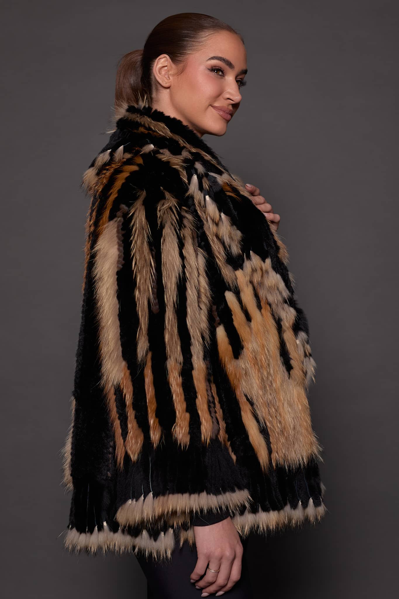 SASCHA REX KNIT BLACK SIDE the side of a woman in a black and brown fur knitted jacket against a grey background