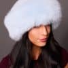 High angle frontal view of a woman in a baby blue mink fur and baby blue fox fur hat standing in front of a grey background.