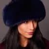 High angle frontal view of a woman in a blue mink fur and blue fox fur hat standing in front of a grey background.