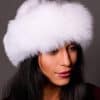 High angle frontal view of a woman in a cross mink fur and arctic fox fur hat standing in front of a grey background.