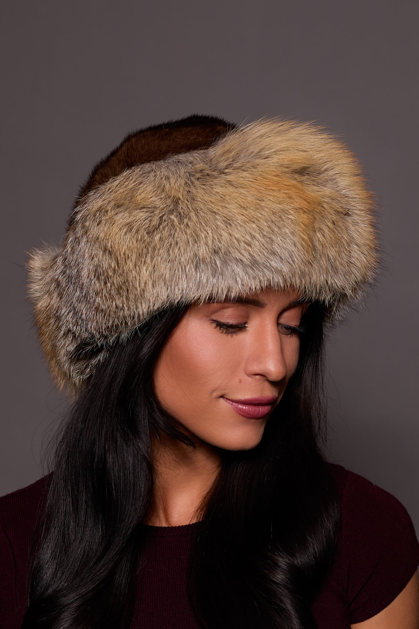 High angle frontal view of a woman in a mahogany mink fur and cross fox fur hat standing in front of a grey background.