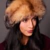 High angle frontal view of a woman in a mahogany mink fur and crystal fox fur hat standing in front of a grey background.