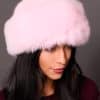 High angle frontal view of a woman in a pink mink fur and pink fox fur hat standing in front of a grey background.