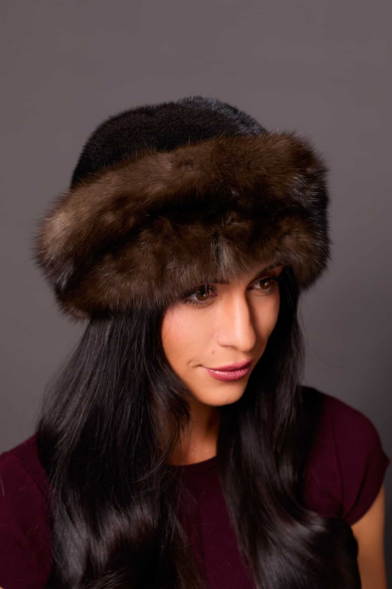 High angle frontal view of a woman wearing a ranch mink fur and Russian sable fur hat standing in front of a grey background.