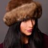 High angle frontal view of a woman wearing a sheared mink fur and Russian sable fur hat standing in front of a grey background.