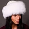 High angle frontal view of a woman in a white mink fur and arctic fox fur hat standing in front of a grey background.