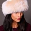 High angle frontal view of a woman in a white mink fur and blush fox fur hat standing in front of a grey background.